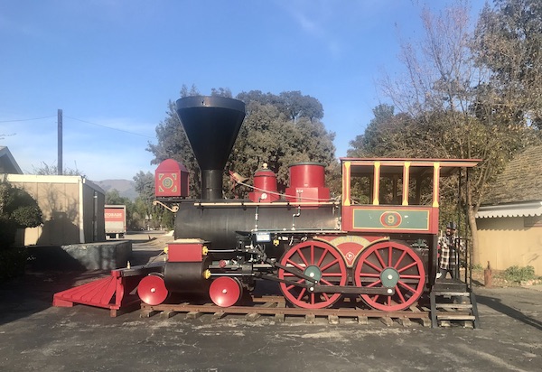 An old red locomotive on a short track with trees and blue sky at Casa de Fruta Hollister California