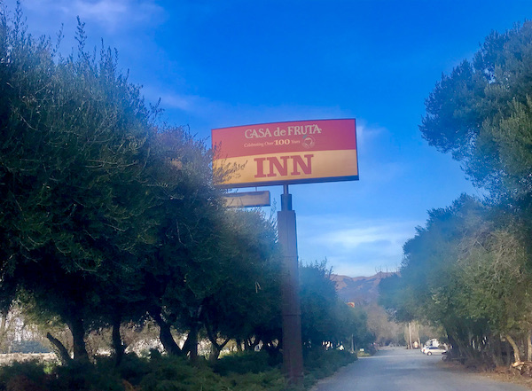 A large red and yellow sign above a row of trees and lots of blue sky at Casa de Fruta Hollister California