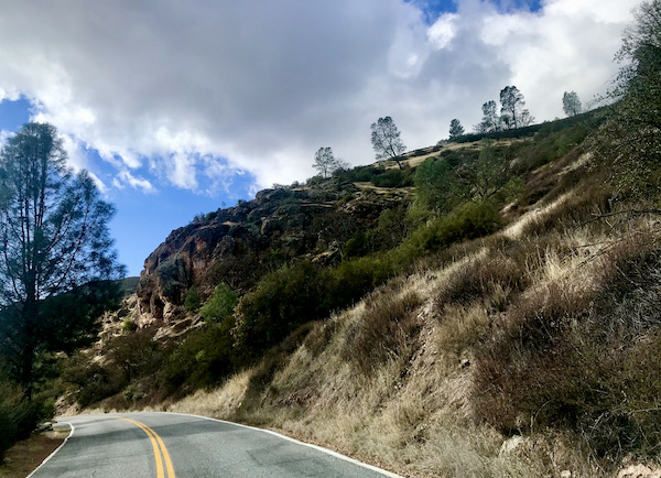 A mountain road with trees and cloudy blue sky found while Exploring Hollister California and Beyond