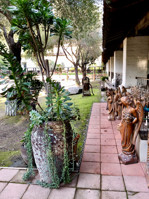 A garden with a tiled patio and a line of religious statues lining the patio found while Exploring Hollister California and Beyond