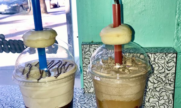 Two milkshakes sitting on a black and white counter in front of a mint green wall at ￼