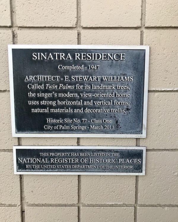 A cream brick wall with a plaque giving the home behind the wall historic designation near Great Shakes in Palm Springs California