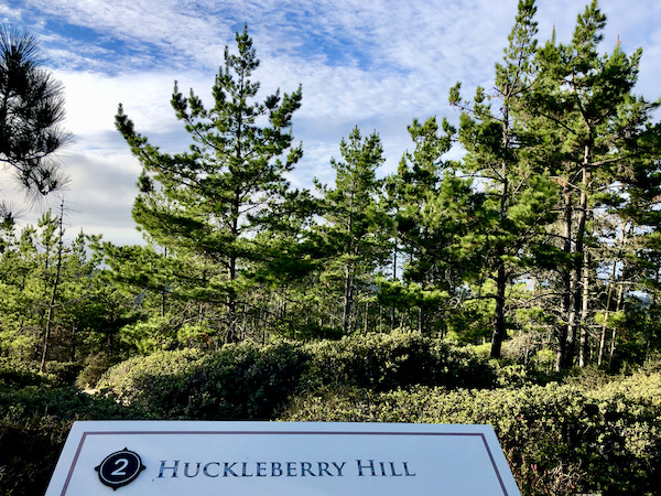 A white sign designates the area as Huckleberry Hill with trees behind the sign along Scenic 17-mile Drive Monterey California