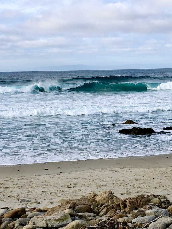 Sandy beach with ocean waves crashing against rocks in the water along the Scenic 17-mile Drive Monterey California