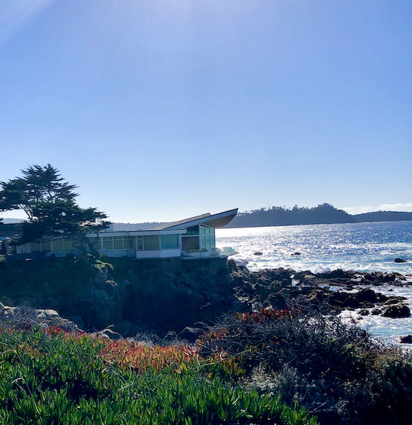 A white house with a jutting roof, lawn, rocks and ocean near the Scenic 17-mile Drive Monterey California