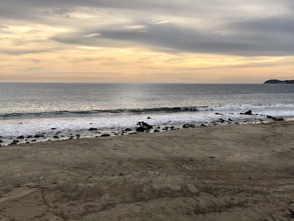 Beach, ocean, small rocks at the edge of the ocean and stormy sky at the Southern California Coast