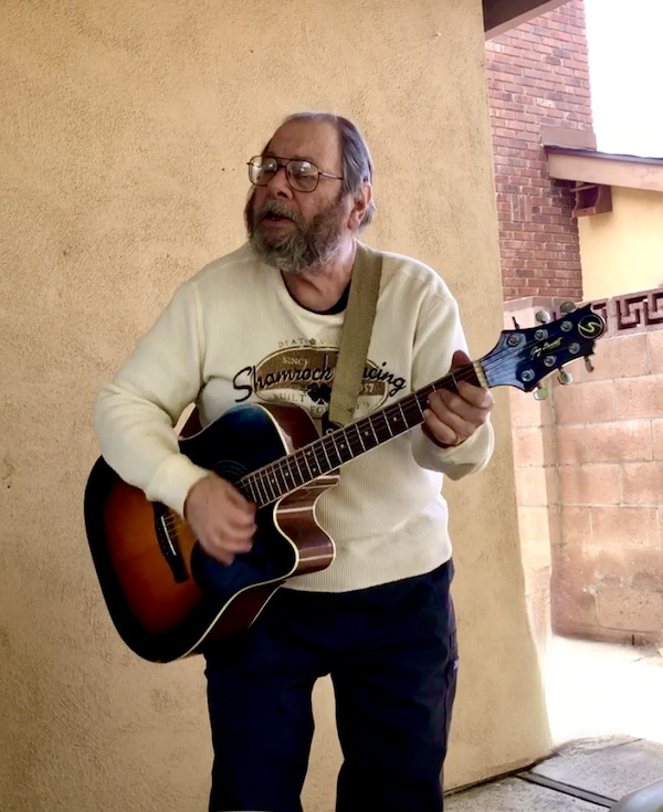A man wth a beard playing guitar and singing near the Southern California Coast