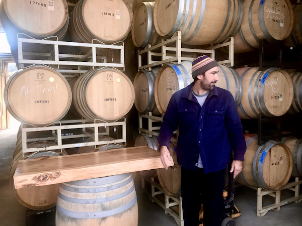 A man with a knit cap standing by stacks of wine barrels seen on our tour Behind the Scenes at Stuhlmuller Vineyards