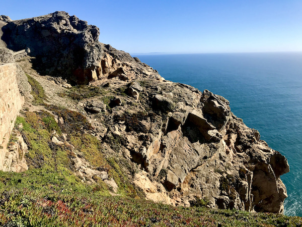 Craggy mountain with a wedge of ocean on right and blue sky at the Historic Point Reyes Lighthouse