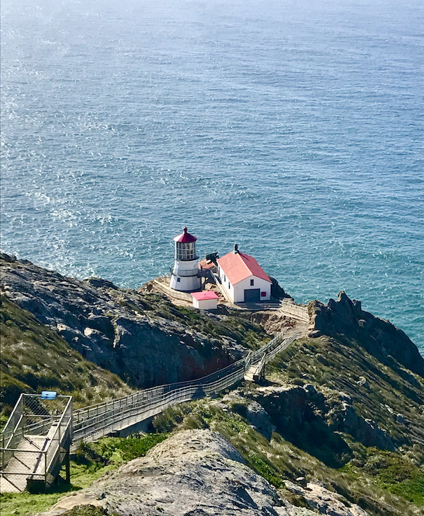 A long path with railings leading to the Historic Point Reyes Lighthouse and lots of blue ocean.