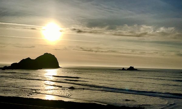 Sun setting on dark gray ocean with rocks near Jedediah Smith Redwoods Crescent City CA