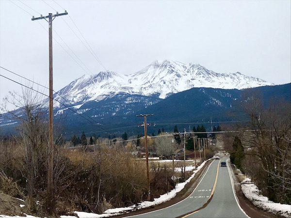 A highway with snow and bushes on either side and snow covered mountain in the distance at Mt. Shasta and Shasta Lake California