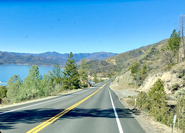 A road with lake on left and mountains in the distance near Mt. Shasta and Shasta Lake California