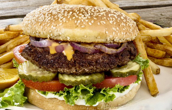A burger in a sesame seed bun with white sauce, lettuce, tomato, pickles, cheese and red onion near Mt. Shasta and Shasta Lake California