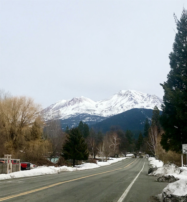 A highway leading to a snow covered mountain and gray sky near Mt. Shasta and Shasta Lake California