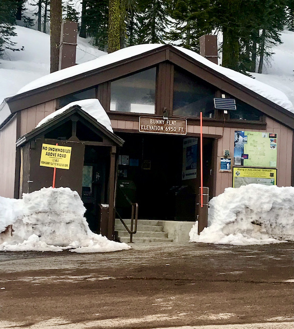 A brown building with snow on the roof and two piles of snow in front at Mt. Shasta and Shasta Lake California