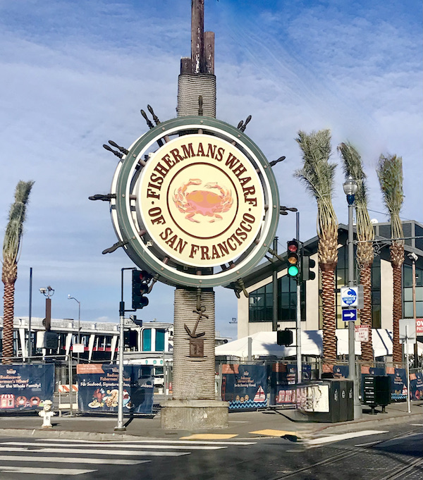 A large sign that looks like a ships wheel welcomes you to Fishermans Wharf in San Francisco California