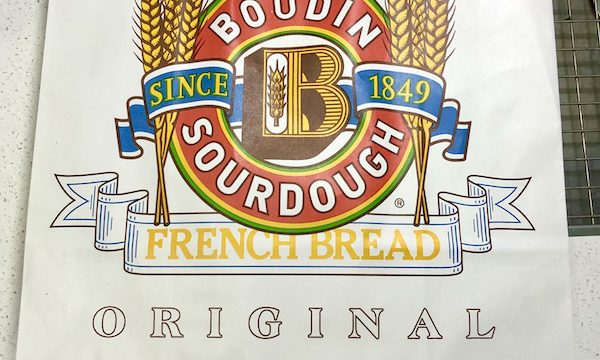 A white shopping bag with the Boudin Bakery logo in god and red from San Francisco California