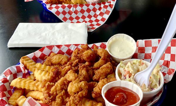 A pair of baskets lined with red and white checkered paper filled with golden fried clam strips and French Fries, coleslaw, cocktail and tartar sauces at The Hungry Clam Brookings Oregon