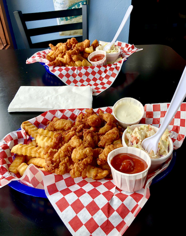 A pair of baskets lined with red and white checkered paper filled with golden fried clam strips and French Fries, coleslaw, cocktail and tartar sauces at The Hungry Clam Brookings Oregon
