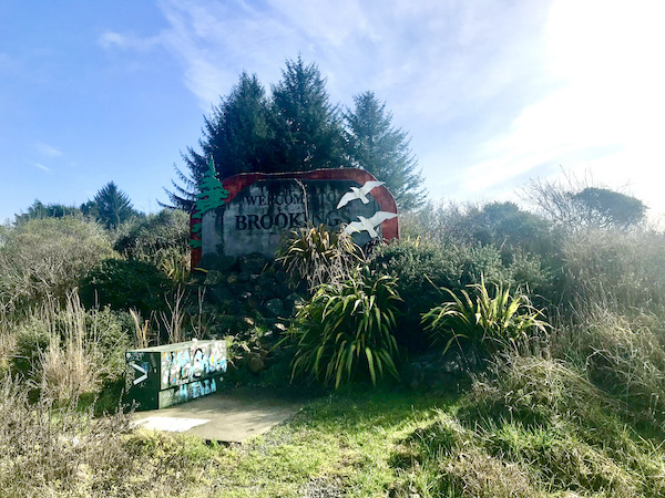 A cluster of bushes trees with a Welcome to Brookings sign near The Hungry Clam Brookings Oregon