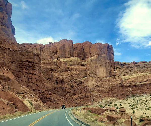 A fortress like rock formation with paved road running passed it at Arches National Park Moab Utah