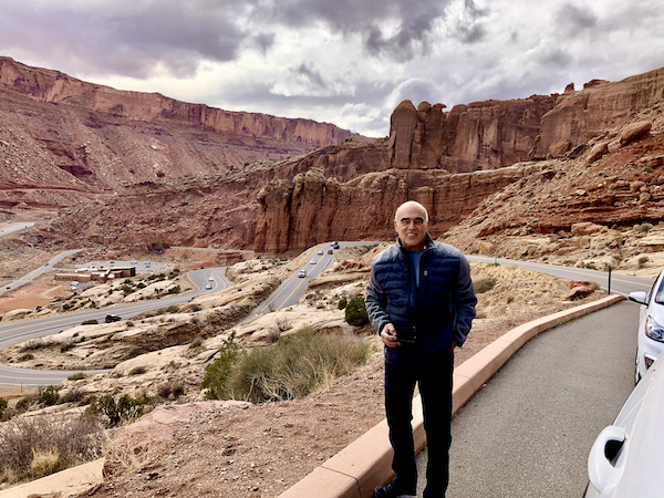 A man standing by the side of a road through mountains at Arches National Park Moab Utah