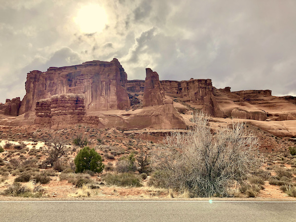 Sun shining behind gray clouds above angular red rock mountains in Arches National Park Moab Utah