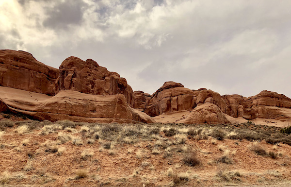 Desert with small green plants a the foot of red rock mountains in Arches National Park Moab Utah