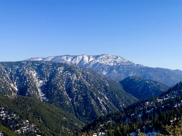 Tree covered mountains in the foreground and snow covered mountain in the distance at Big Bear Lake California
