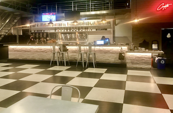A restaurant interior with black and white checkered floor and long white stone bar. The restaurant is Coyote Sonoma in Healdsburg CA
