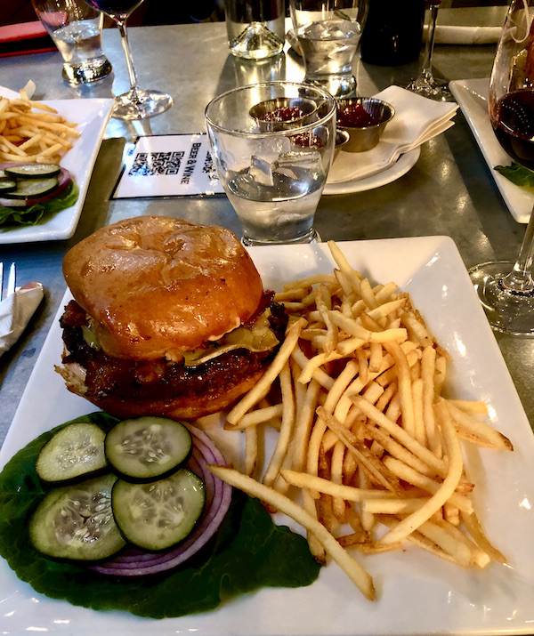 A larges square white plate topped with a bacon cheeseburger, fries and pickles at Coyote Sonoma in Healdsburg CA