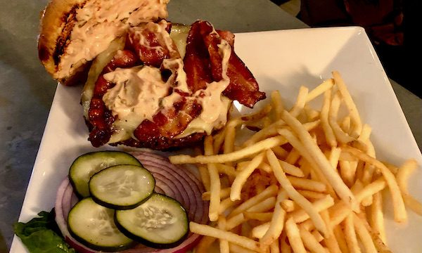 A bacon cheeseburger on a white plate with pickles and fries at Coyote Sonoma in Healdsburg CA