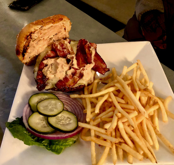 A bacon cheeseburger on a white plate with pickles and fries at Coyote Sonoma in Healdsburg CA