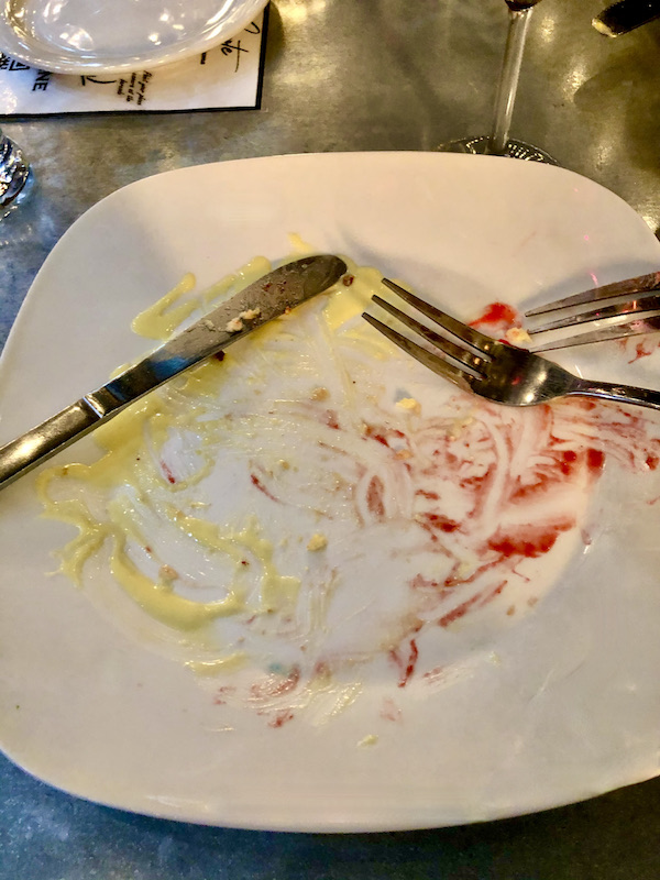 A white plate with remnants of creme anglaise and raspberry, two forks and a knife at Coyote Sonoma in Healdsburg CA