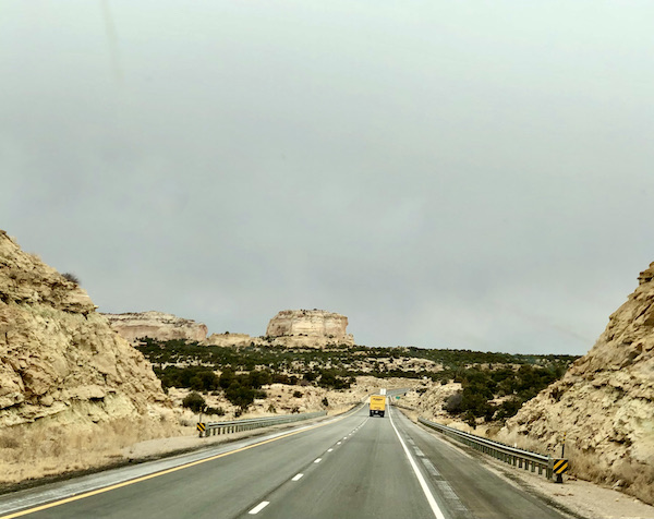 A highway flanked by mountains with lots of trees in the distance on our Scenic Drive to Moab Utah