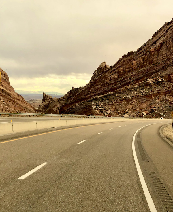 A road curves passed a deep red mountain on our Scenic Drive to Moab Utah