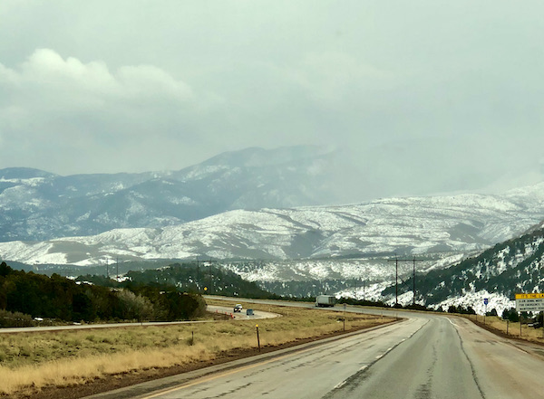 Highway and mountains with snow and clouds in the distance along our Scenic Drive to Moab Utah