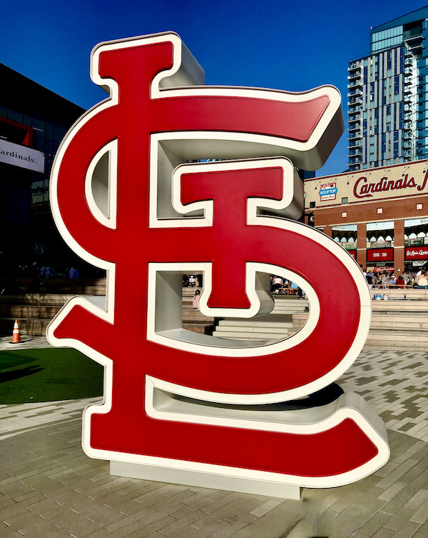A red and white sculpture of the letters ST and L intertwined. This stands on the sidewalk outside of Busch Stadium in Downtown St. Louis Missouri