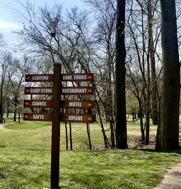 A directional sign on a lawn with lots of trees at Meramec Caverns Stanton Missouri