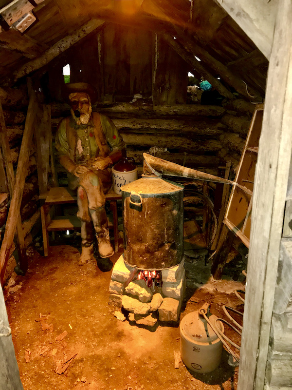 Inside a shack with a moonshine still and statue of a man.