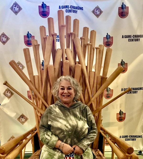 A backdrop of many baseball bats and a woman in a tie die sweatshirt at the Negro Leagues Baseball Museum