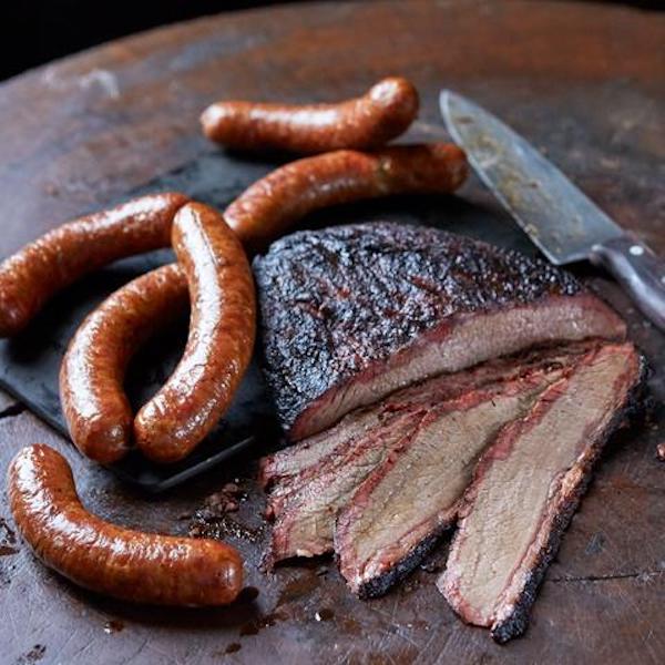 A cutting board topped with a knife, sliced meat and sausage links.