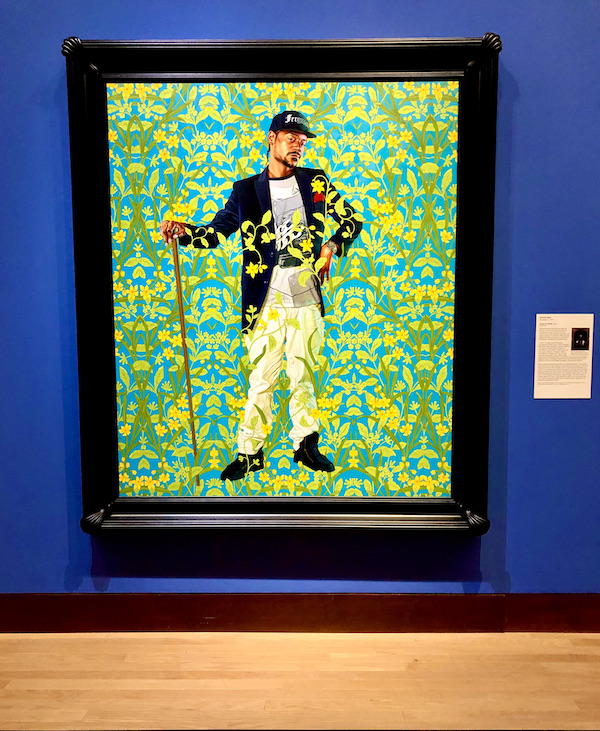 A portrait of a man with a walking stick agains a green print background at the Oklahoma City Museum of Art