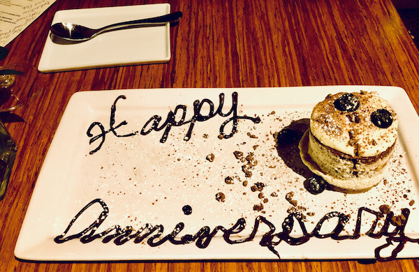 A rectangular white plate with a round portion of tiramisu and Happy Anniversary written in chocolate at Stella Modern Italian Cuisine OKC