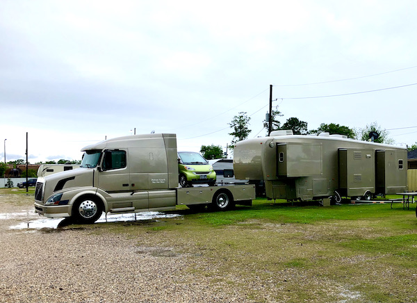 A tan semi truck with a lime green Smart car in the bed and a tan 5th Wheel. Seen while Back in NOLA for a Month