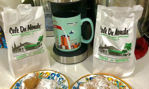 Two white bags with plates in front of each topped with fried dough squares enjoyed while Back in NOLA for a Month