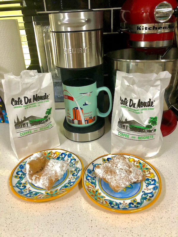 Two white bags with plates in front of each topped with fried dough squares enjoyed while Back in NOLA for a Month