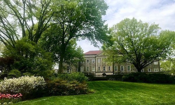 A mansion seen through trees with vast lawn in front.