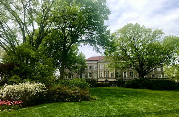 A mansion seen through trees with vast lawn in front.